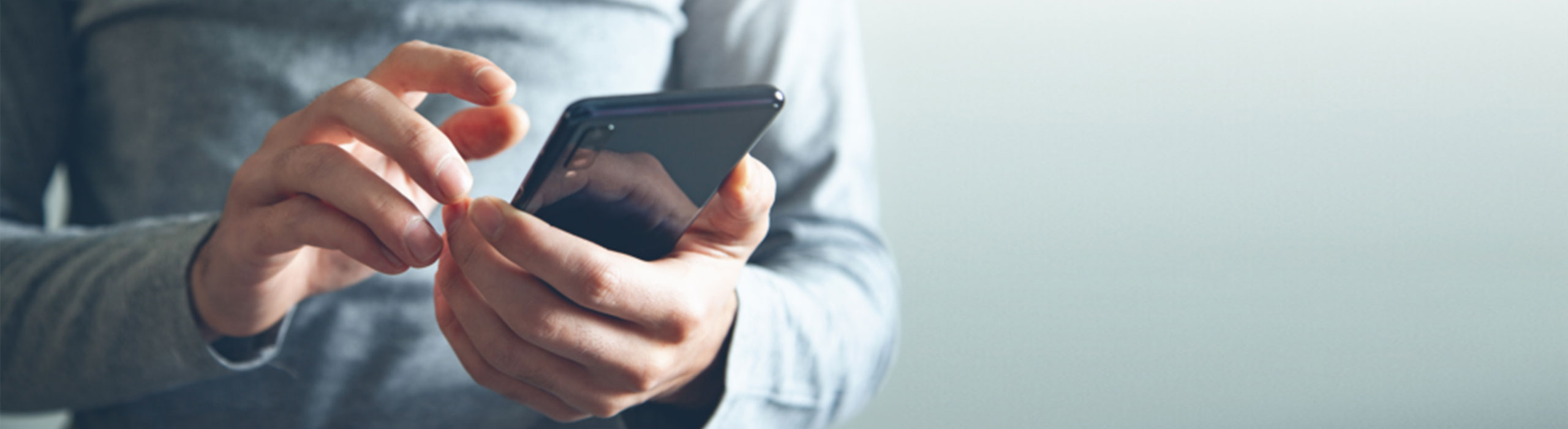 Ein Mann im blauen Pullover hält ein Smartphone.