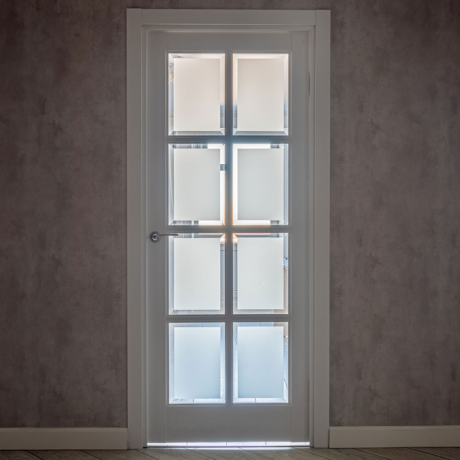 Eine weiße Eingangstür, die sechs kleine Glasfenster besitzt, durch die das Tageslicht scheint.